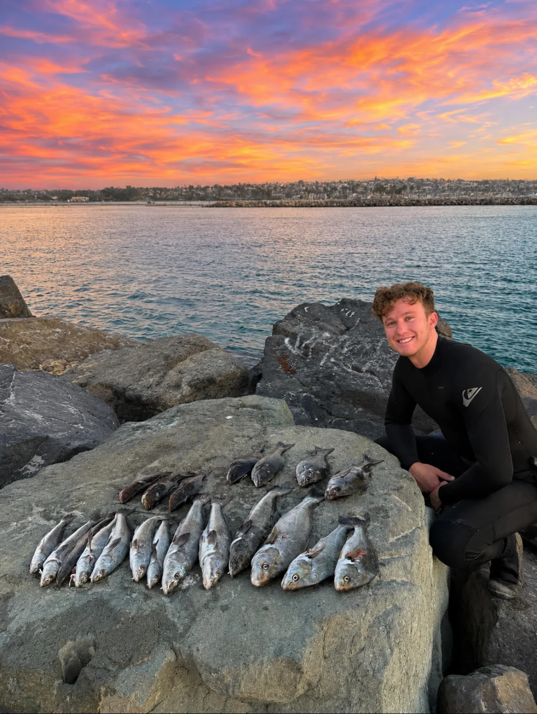 Nick in a wetsuit on the jetty rocks at sunset with a day's catch of fish laid out