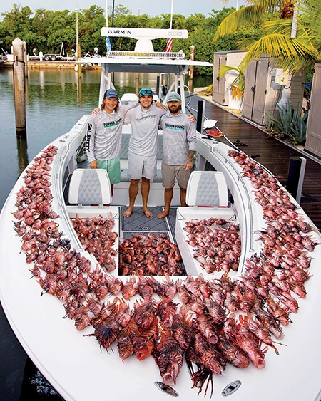 The Forever Young crew stands on the bow of a boat lined edge to edge with hundreds of speared lionfish.